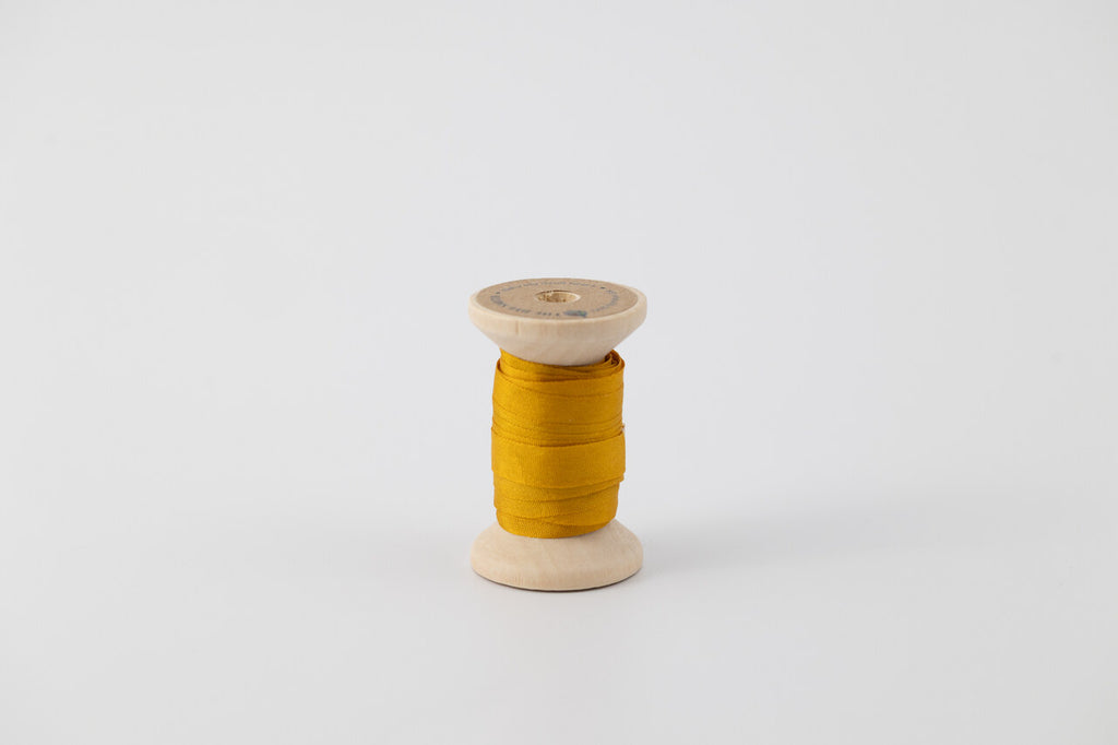 A spool of naturally dyed silk ribbon dyed with marigold to a golden yellow color.