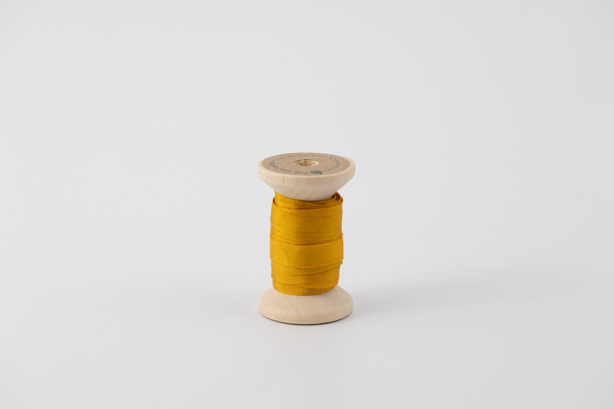 A spool of naturally dyed silk ribbon dyed with marigold to a golden yellow color.