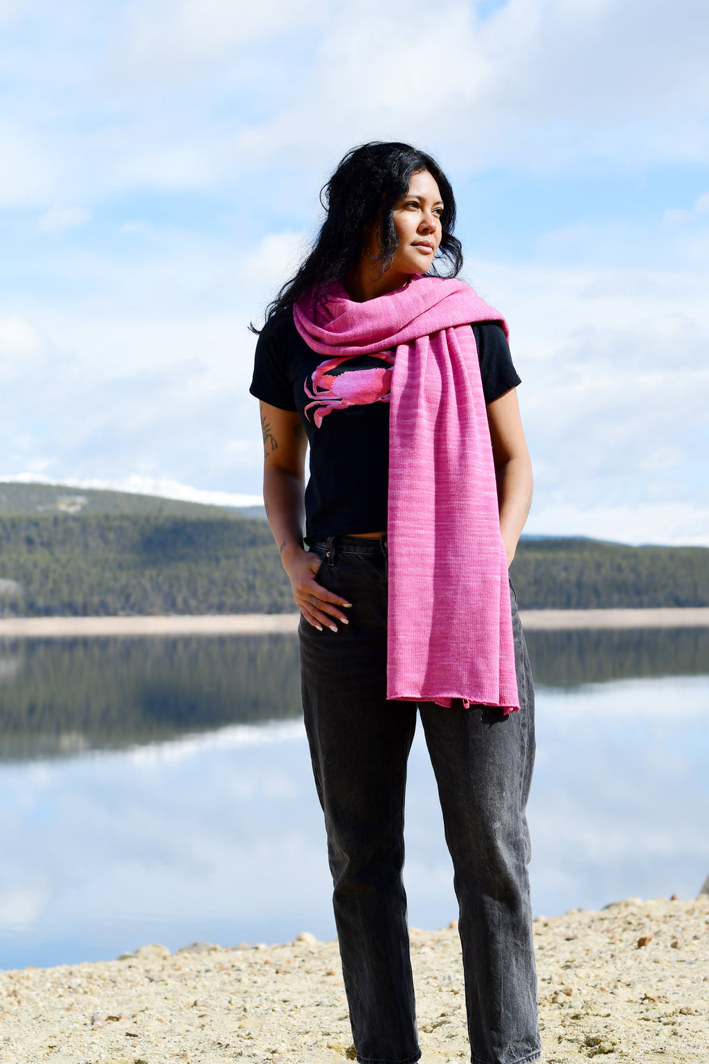 A woman wearing a pink scarf that is made of merino and silk and naturally dyed with cochineal.