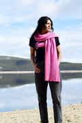 A woman wearing a pink scarf that is made of merino and silk and naturally dyed with cochineal.